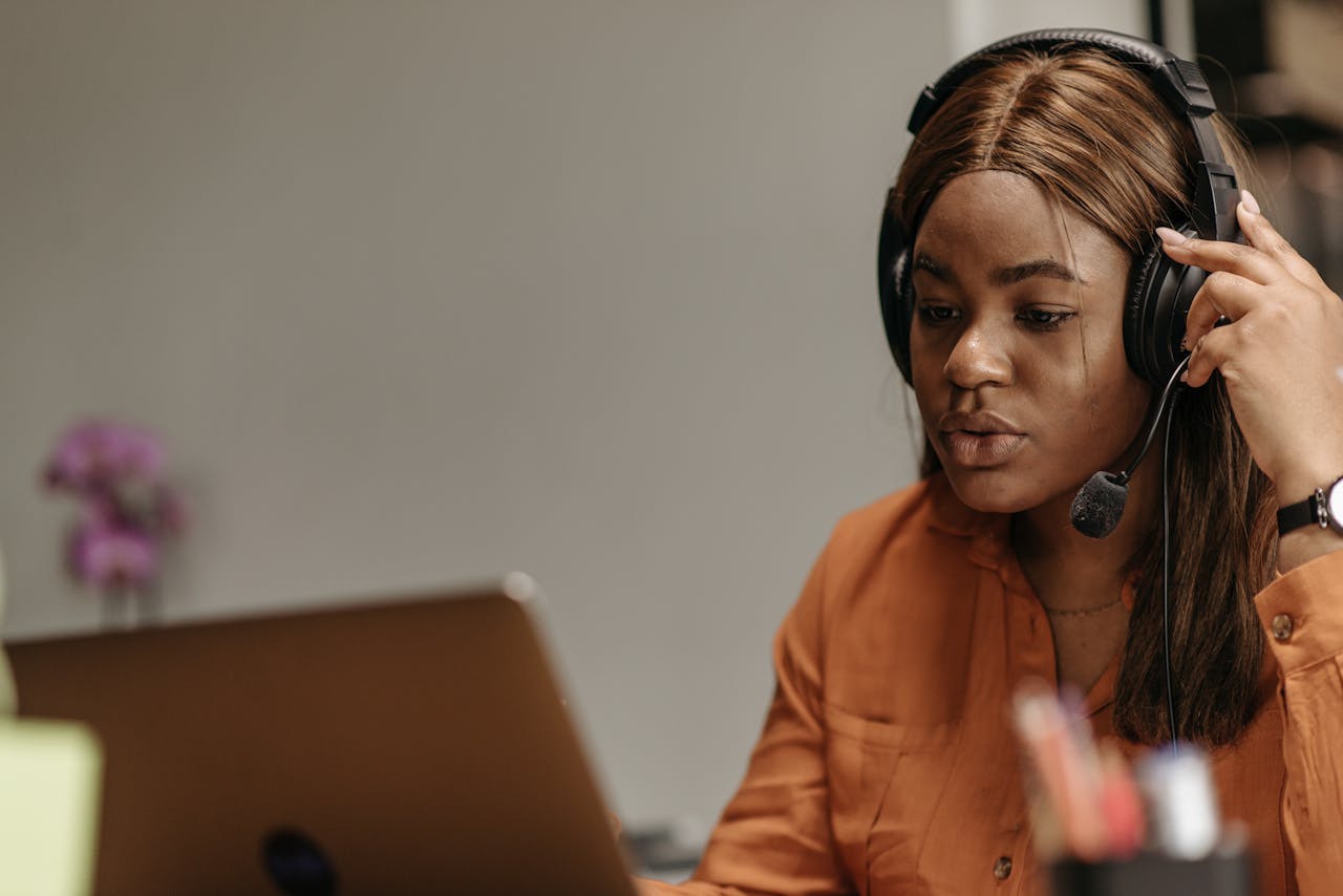 Home African American woman working in customer support with headphones and laptop indoors.